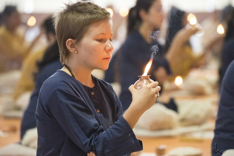 A young girl practicing Bhuta Shuddhi by lighting a candle in front of a group of people during a yoga session.