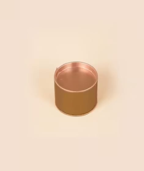 A small, round, open-top metal container with a copper finish on a light beige background.