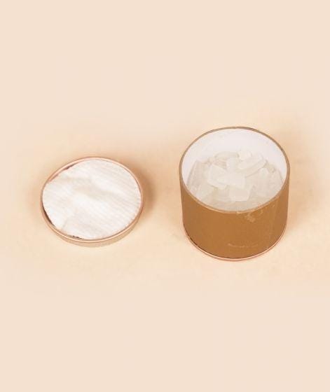 Round cardboard container with white rectangular pieces inside, next to its lid on a light beige background.