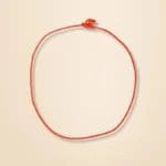 A simple red string tied in a knot forming a circle on a beige background.