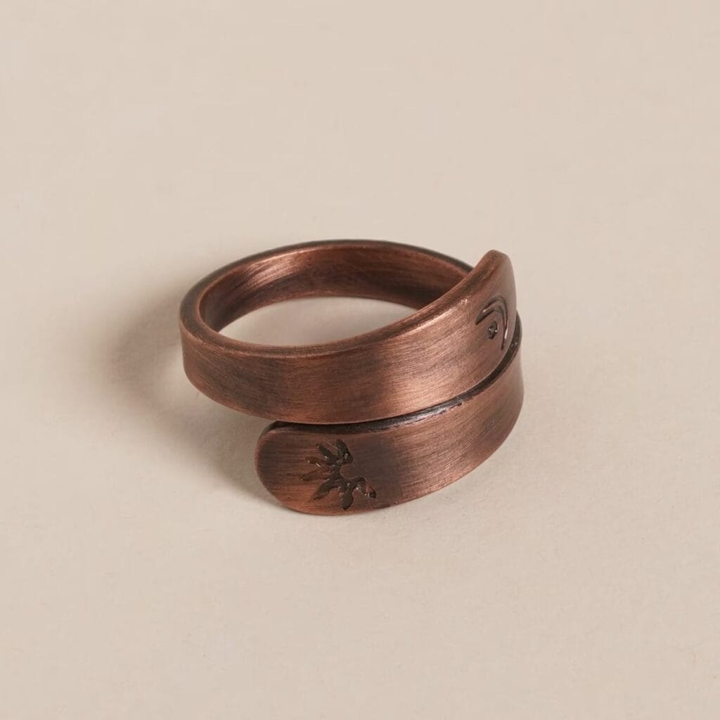 Bronze wrap-around ring with textured surface and engraved designs on both ends, displayed against a plain background.