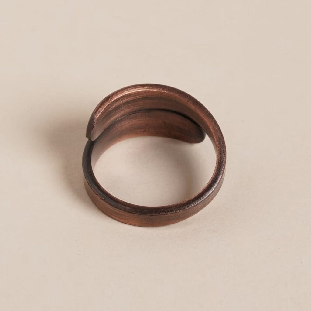 Bronze-colored open ring with a smooth, curved design on a light beige background.