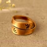 Two bronze rings with engraved symbols, including a crescent and a sun, intertwined on a textured surface.